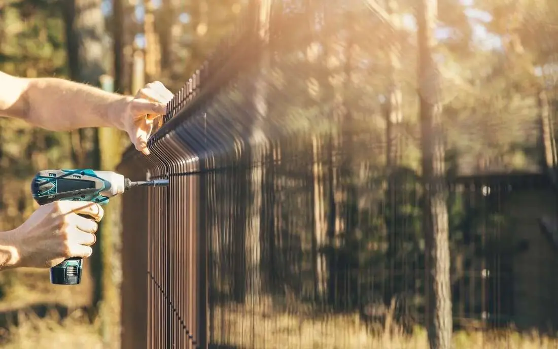Fence installer securing a metal fence panel with a power drill